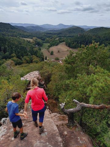 Erwachsene Person und Kind stehen von hinten fotografiert auf einer Felsplatte über dem Bärenbrunnertal, darunter Wald und Wiesen