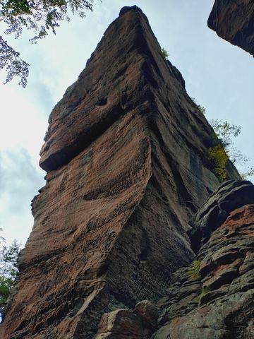 Von unten fotografierter, wabenartig verwitterter Sandsteinturm, der senkrecht in den Himmel steht