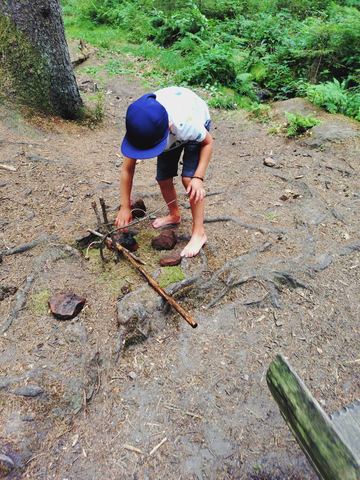 Kind hockt auf dem Waldboden und legt Stöcke zusammen
