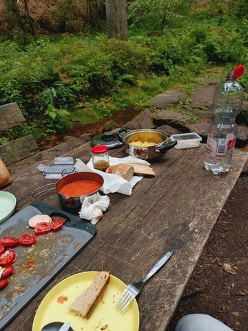 Holztisch mit Pfanne, Topf, Brot, aufgeschnittenen Tomaten und Wasserflaschen