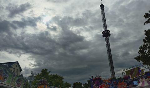 Festplatz des Wurstmarkts mit bunten Fahrgeschäften und einem hohen Kettenkarussell unter einer dunklen Wolkenwand