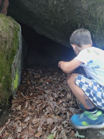 Kind hockt am Eingang einer flachen, mit Laub gefüllten Felshöhle