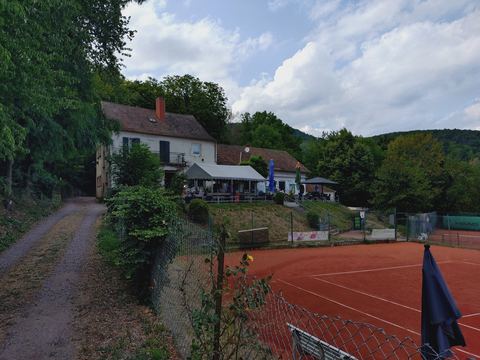 Waldgaststätte mit Terrasse, davor rote Tennisplätze am Waldrand
