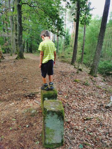 Kind balanciert auf einem alten Grenzstein am Waldweg