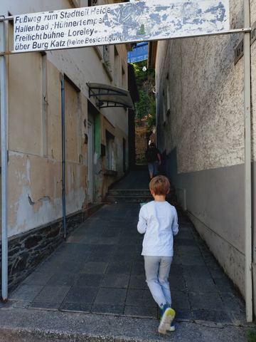 Kind läuft von hinten fotografiert durch eine enge Gasse zwischen zwei Hauswänden auf eine Treppe zu