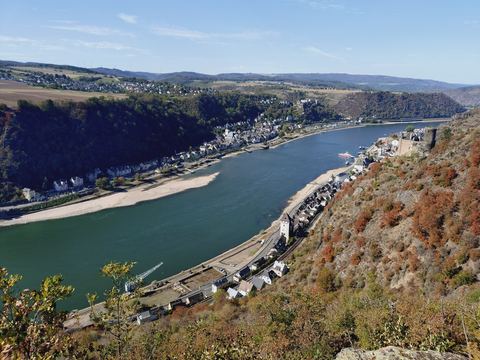 Blick von oben auf St. Goar und St. Goarshausen zu beiden Seiten des Rheins, am rechten Hang eine Burgruine